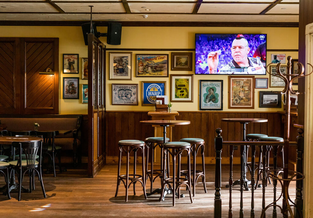 High tables and standing area in The Galway Hooker Irish Pub in Scarborough, Western Australia, with timber paneling, framed artwork, and open circulation space.