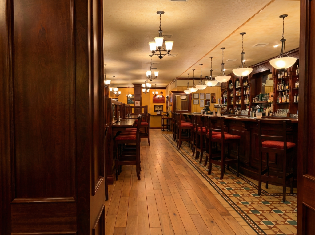 Main bar interior of Grace O’Malley’s Irish Pub in Norfolk, Virginia, featuring dark timber paneling, upholstered bar stools, patterned tile bar edge, and warm pendant lighting.