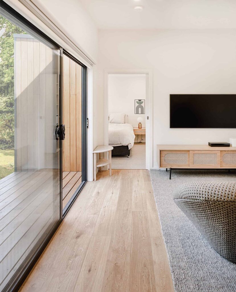 Interior of a modular garden studio showing living area with sliding glass doors, timber flooring, and bedroom beyond, Melbourne, Australia.