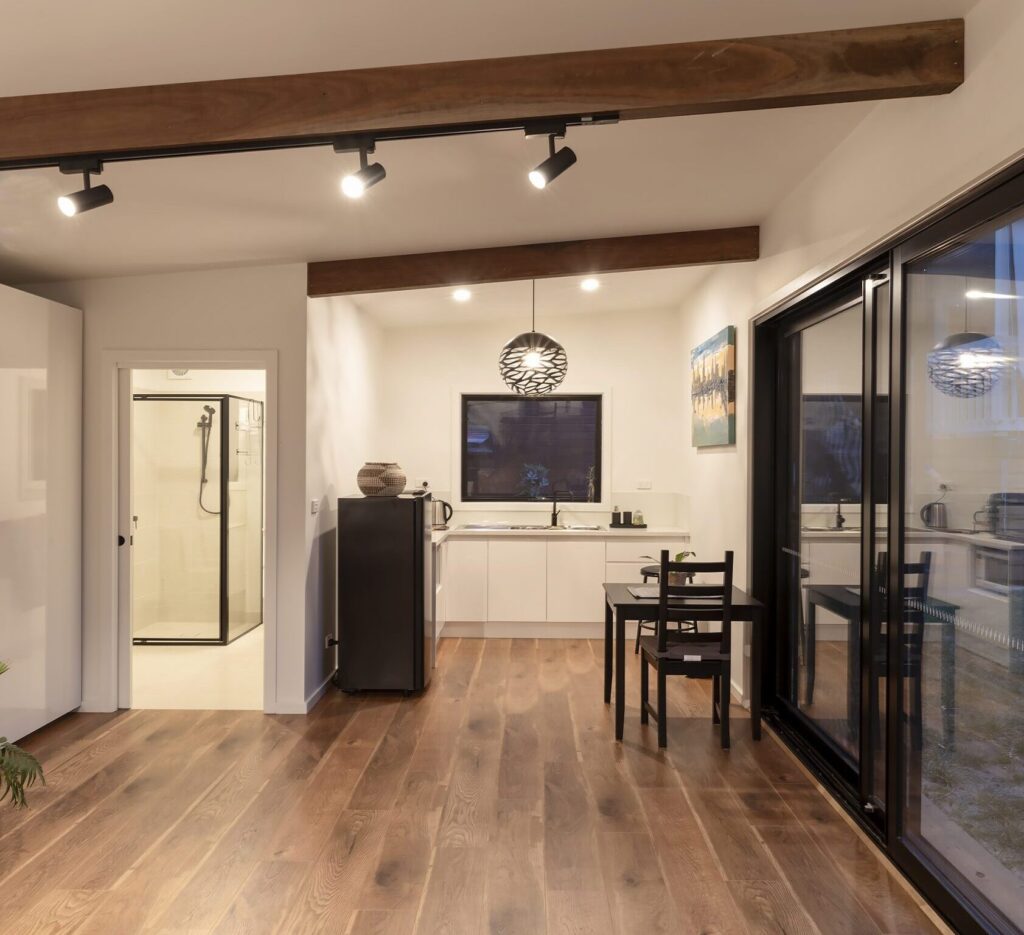 Interior of a compact modular garden studio with timber flooring, kitchenette, bathroom, and sliding glass doors, Melbourne, Australia.