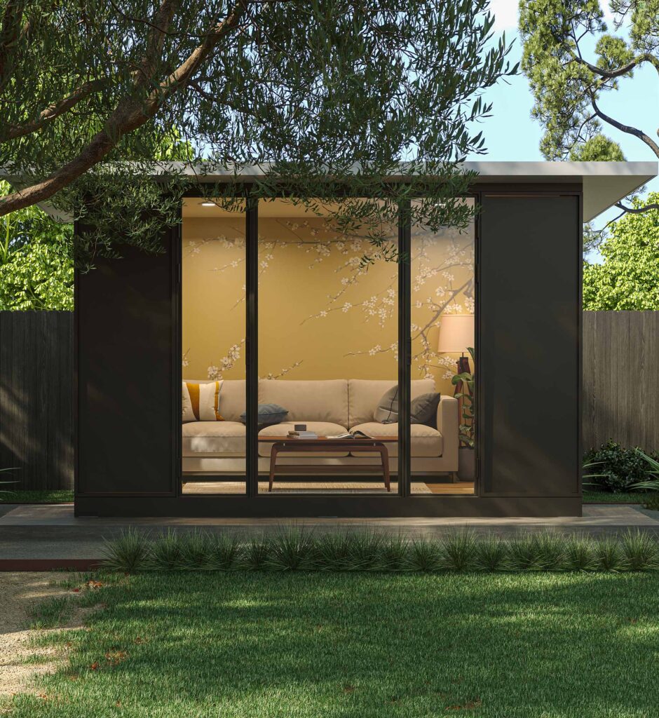 Compact modular office pod in a garden setting, featuring dark cladding, full-height glazing, and a minimalist interior workspace in Melbourne, Australia.
