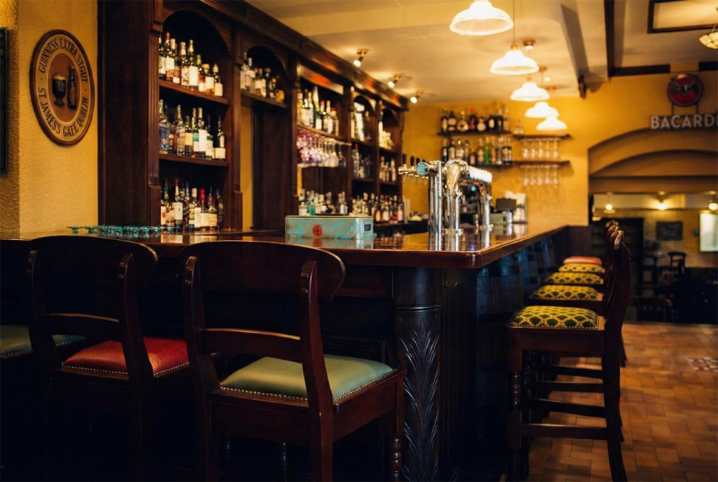 Timber bar counter and back bar shelving at Red Piper gastropub in Vevey, Switzerland, with upholstered bar stools and warm pendant lighting.
