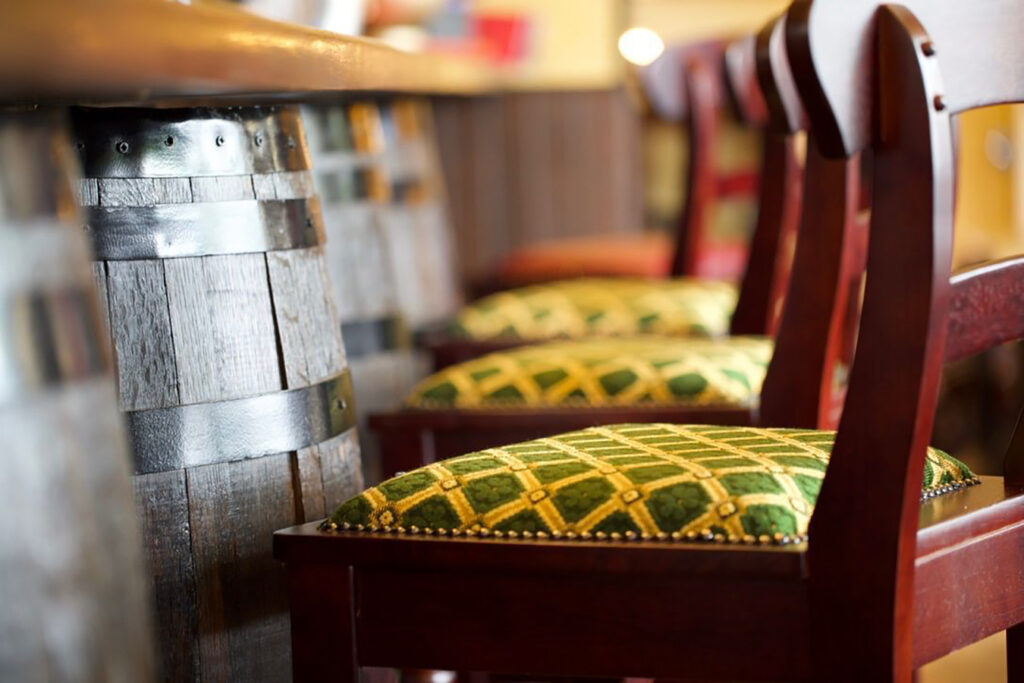 Close-up of reclaimed wooden barrels used as bar front cladding at Red Piper gastropub in Vevey, Switzerland, with upholstered bar stools in the foreground.