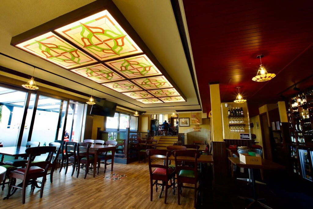 Main dining area with decorative ceiling panels and daylight at Red Piper gastropub in Vevey, Switzerland, showing varied seating and layered lighting.